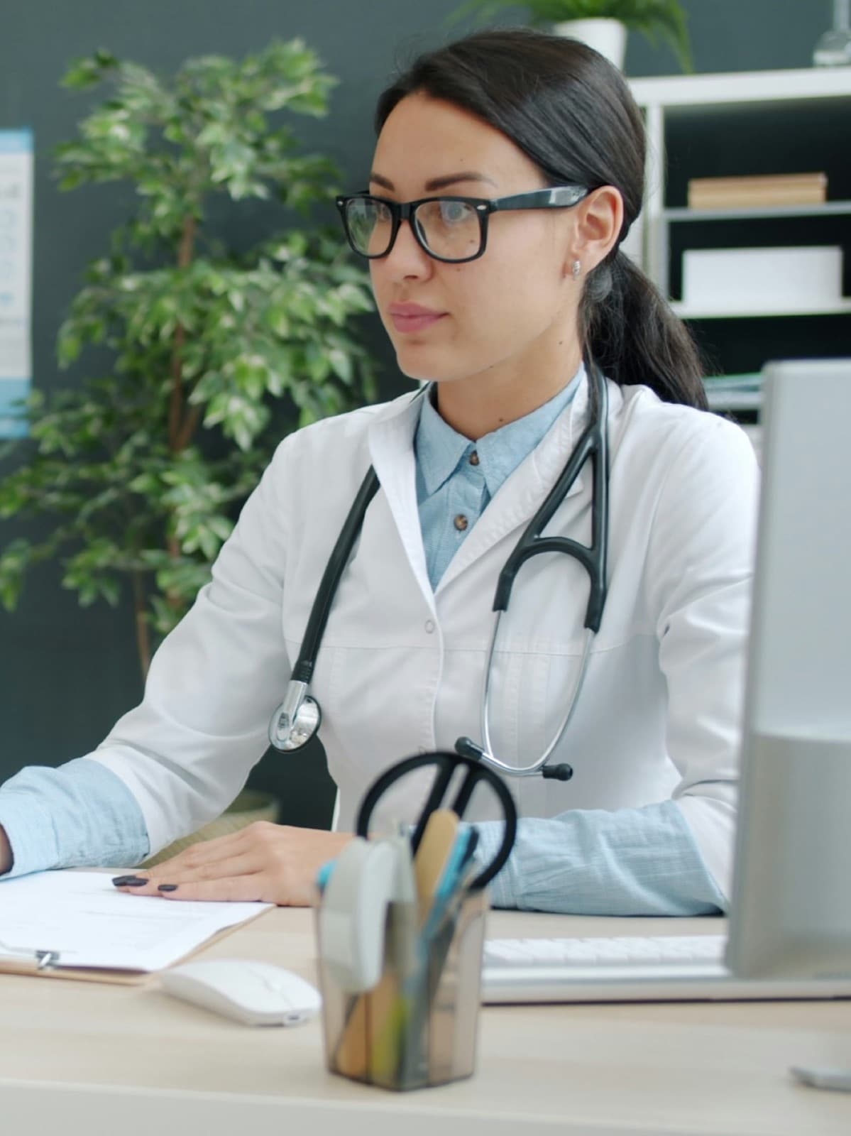 A doctor in a white coat with a patient across her consulting desk
