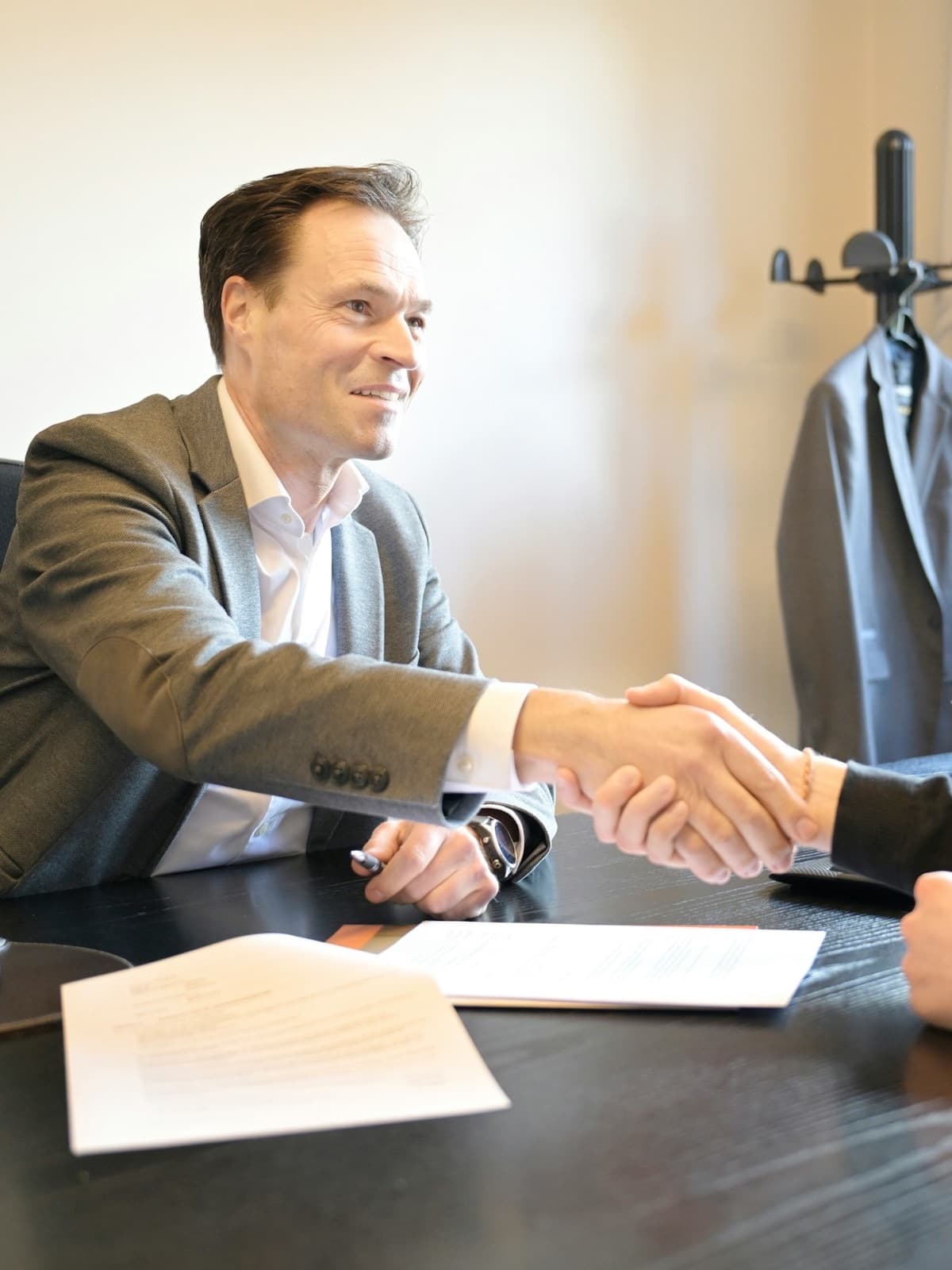 A lawyer in a suit shaking hands with a client across his office desk
